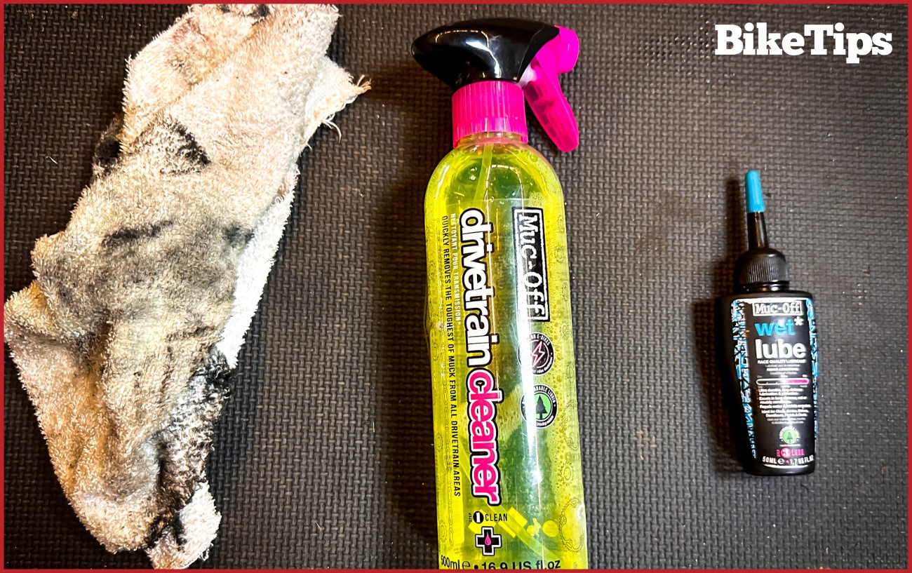 Bike lube, degreaser, and two rags sit on a black floor mat.