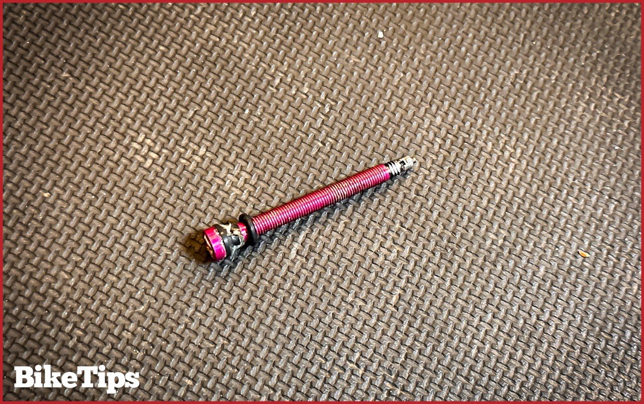 A pink tubeless Presta valve sits on a black surface.