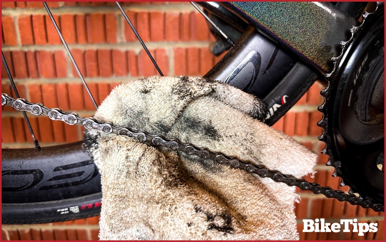 Using a rag to remove grease from a bike chain.