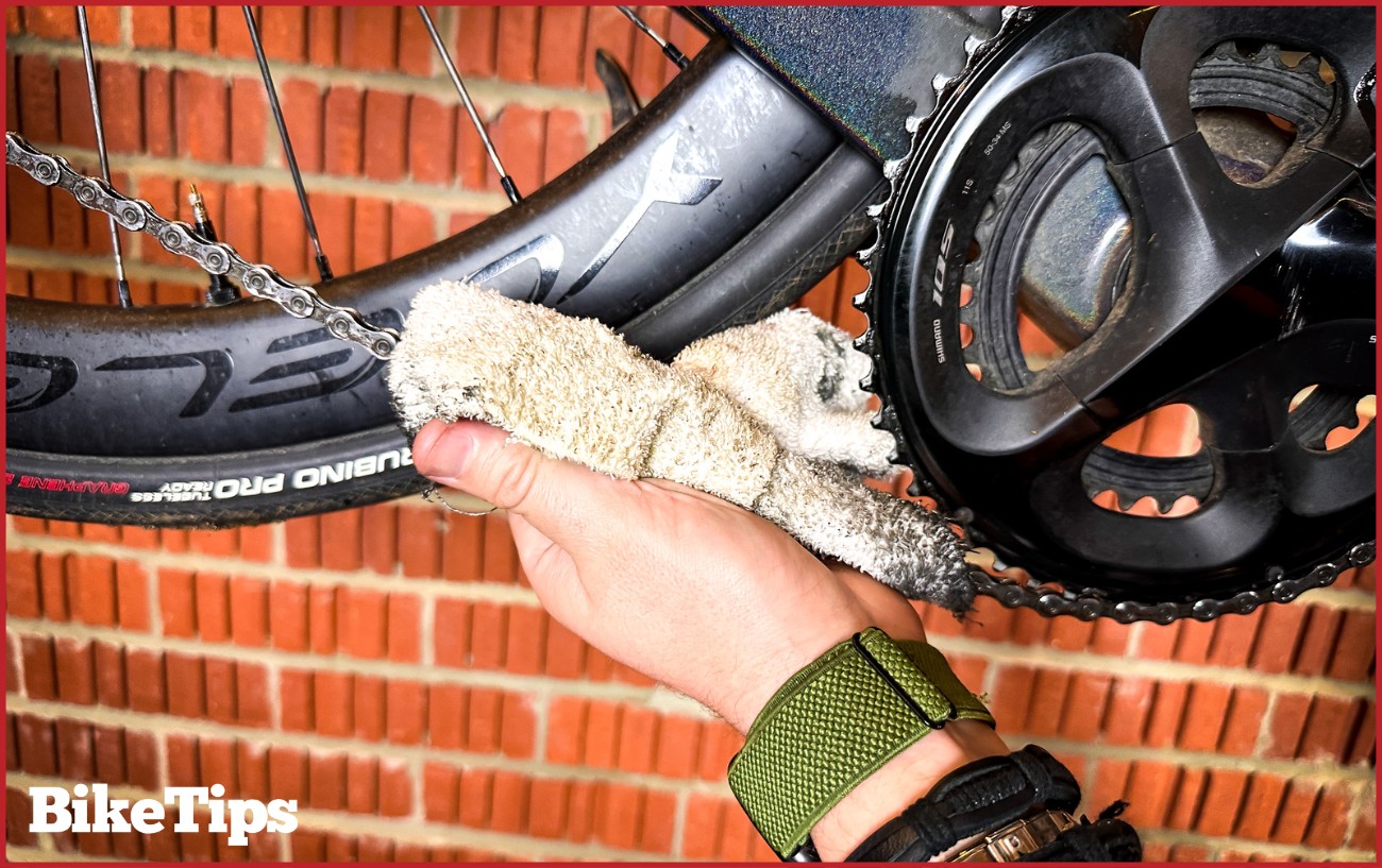 Wiping excess lubricant off the bike chain after application.