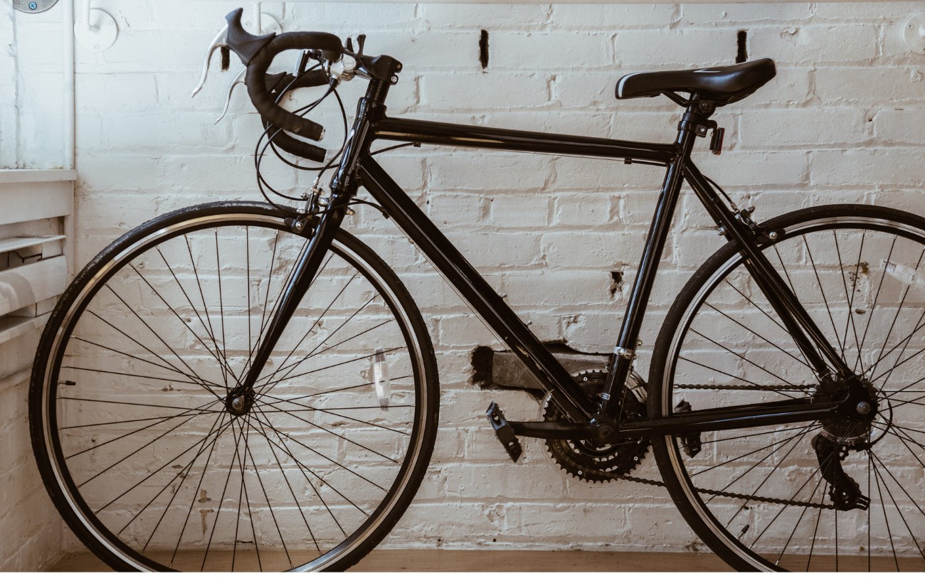 An all-black aluminum road bike against a white brick wall.