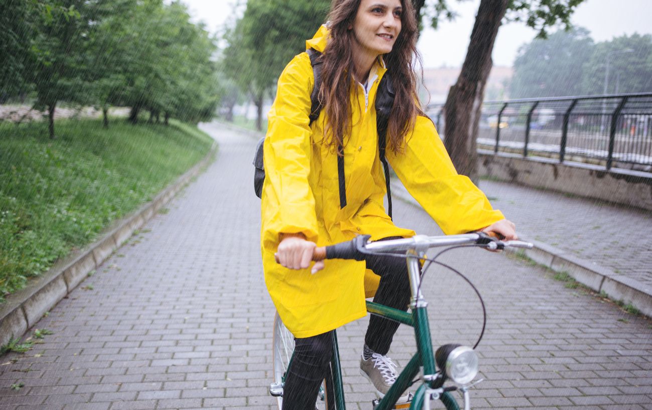 A cyclist in a yellow coat rides in the rain.