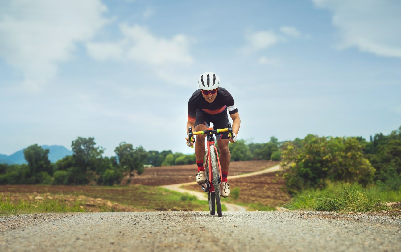 A gravel cyclist climbs a dirt hill on an orange bike.