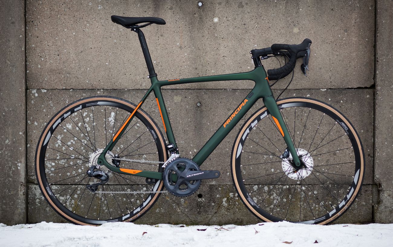 A green road bike leans against a concrete wall in the snow.