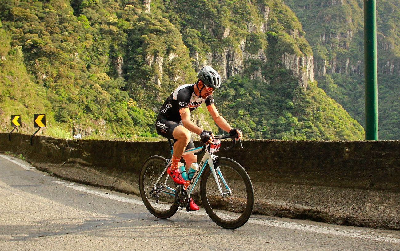 A cyclist climbs a steep hill on a white road bike.