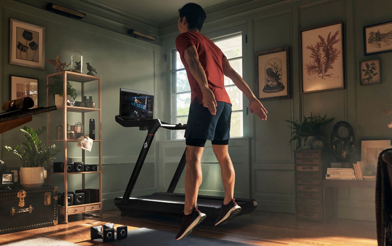 A man performs exercises next to a Peloton treadmill.