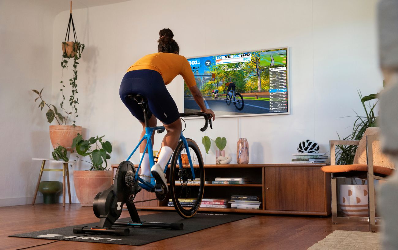 A cyclist uses their Zwift setup in their living room on a blue bike.