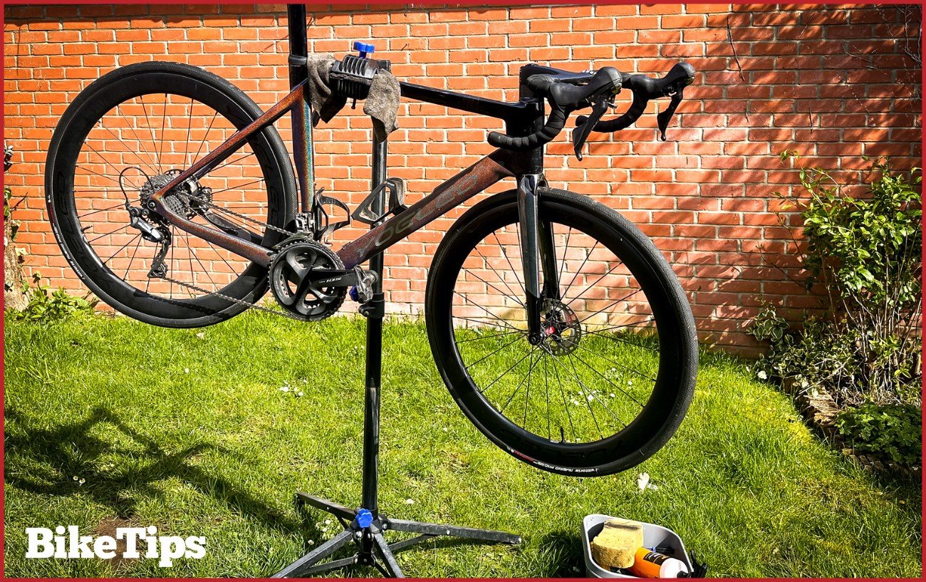 A road bike in a stand ready to be cleaned with the cleaning supplies next to it.
