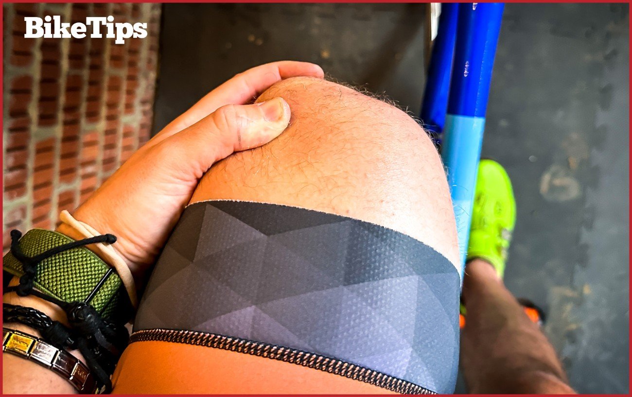 A cyclist on a turbo trainer checking his knee with a green cycling shoe in the background. 