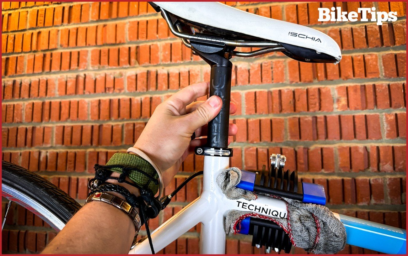 Hand adjusting the seat height on a road bike against a brick wall.