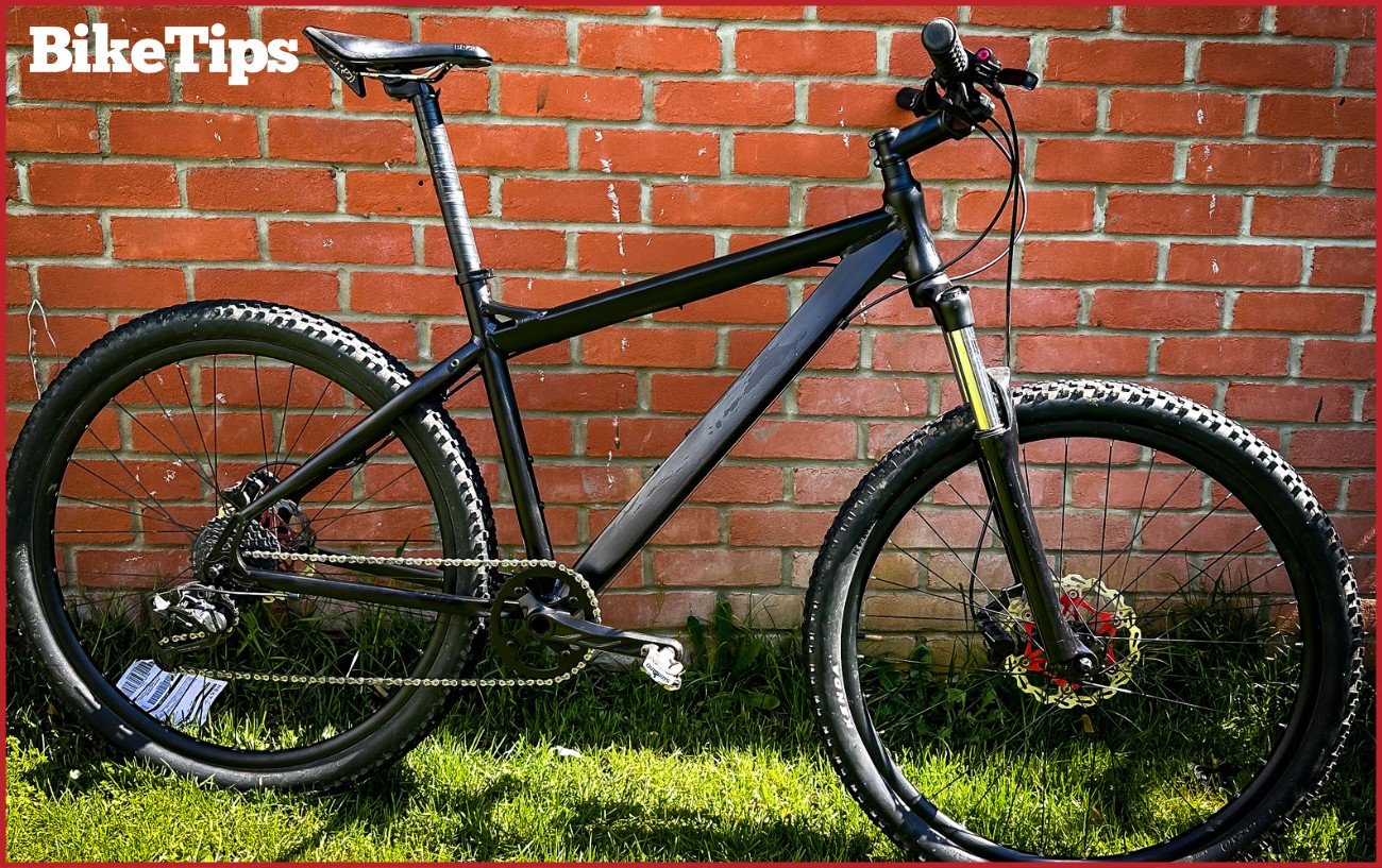 A matte black mountain bike resting against a brick wall.