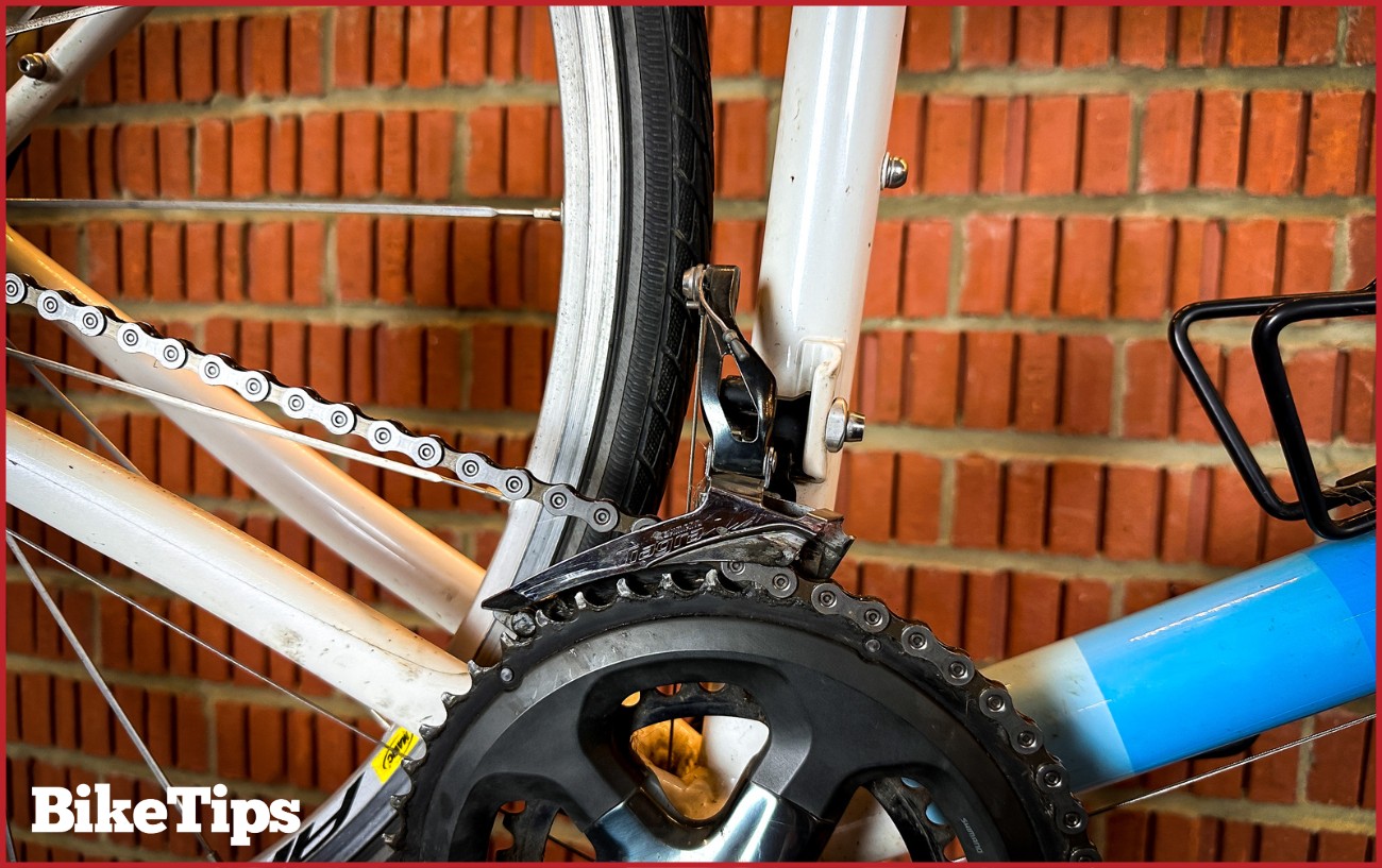 Picture of a Shimano Claris front derailleur against a brick background up close.