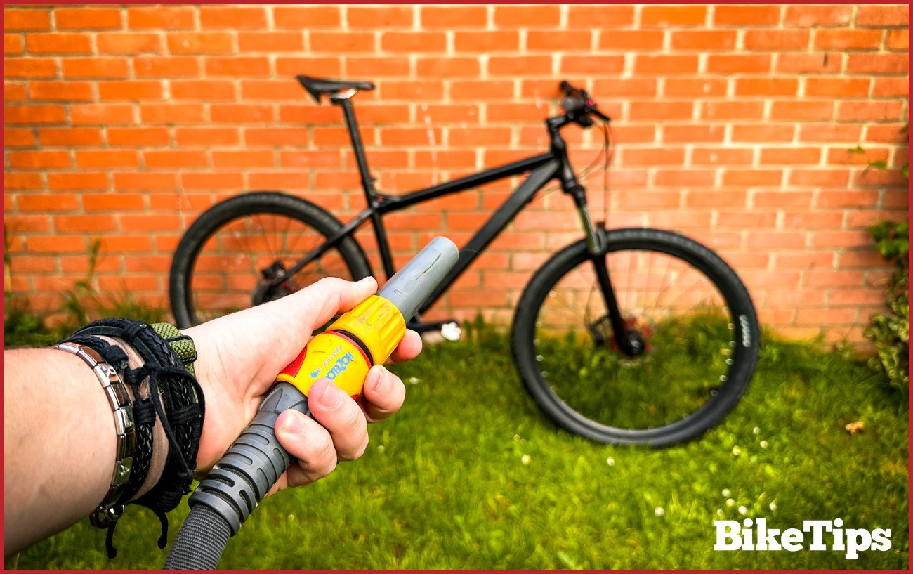 A hose pointing directly at a mountain bike which is about to be washed.