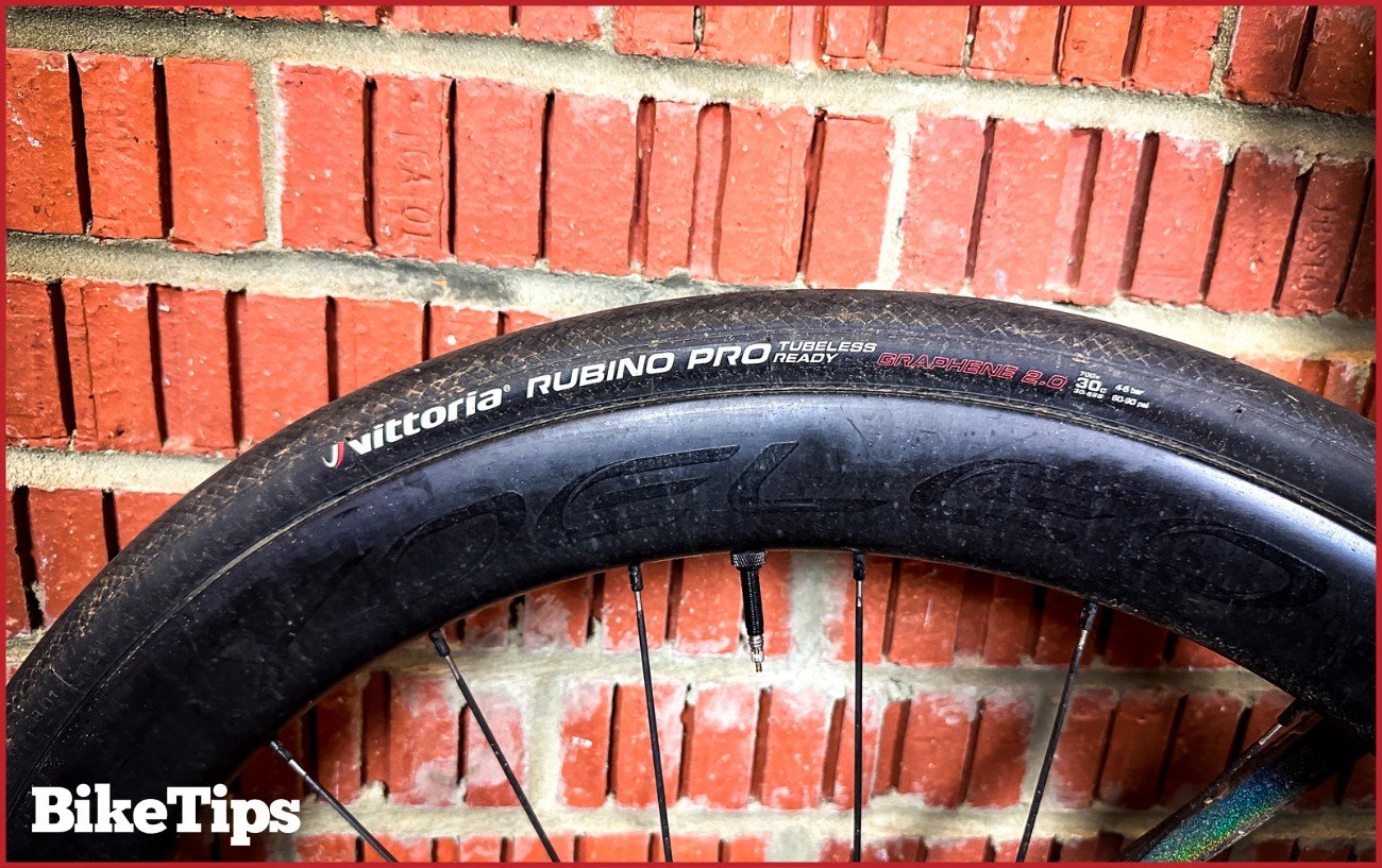 A road bike tire on a deep-section aero wheel leaning against a brick wall.