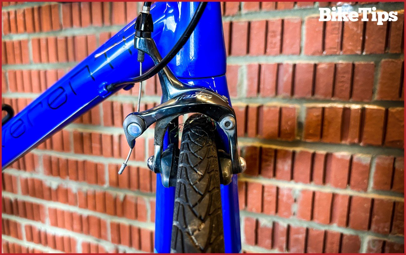 Front view of a Shimano Tiagra front rim brake in front of a brick wall.