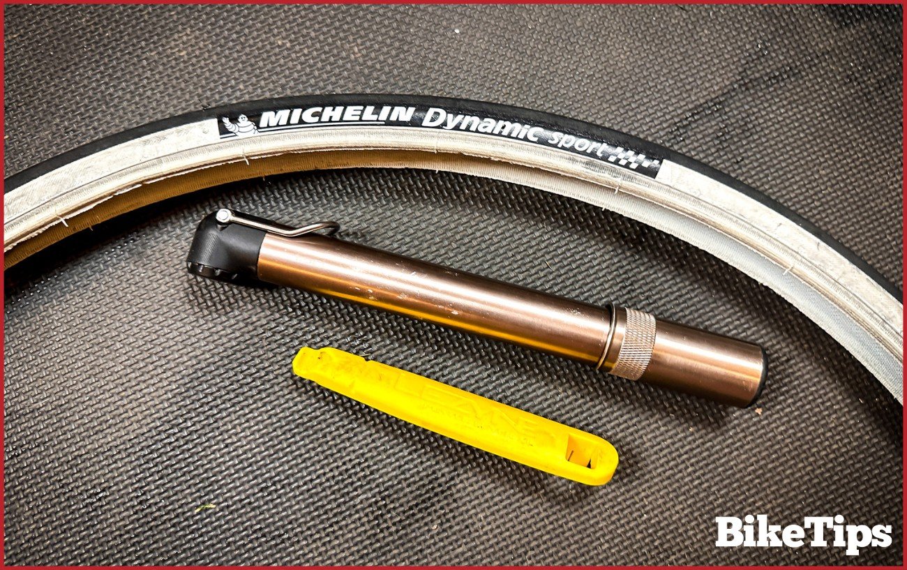 A bike tire, hand pump, and yellow tire lever sit on a black floor mat.