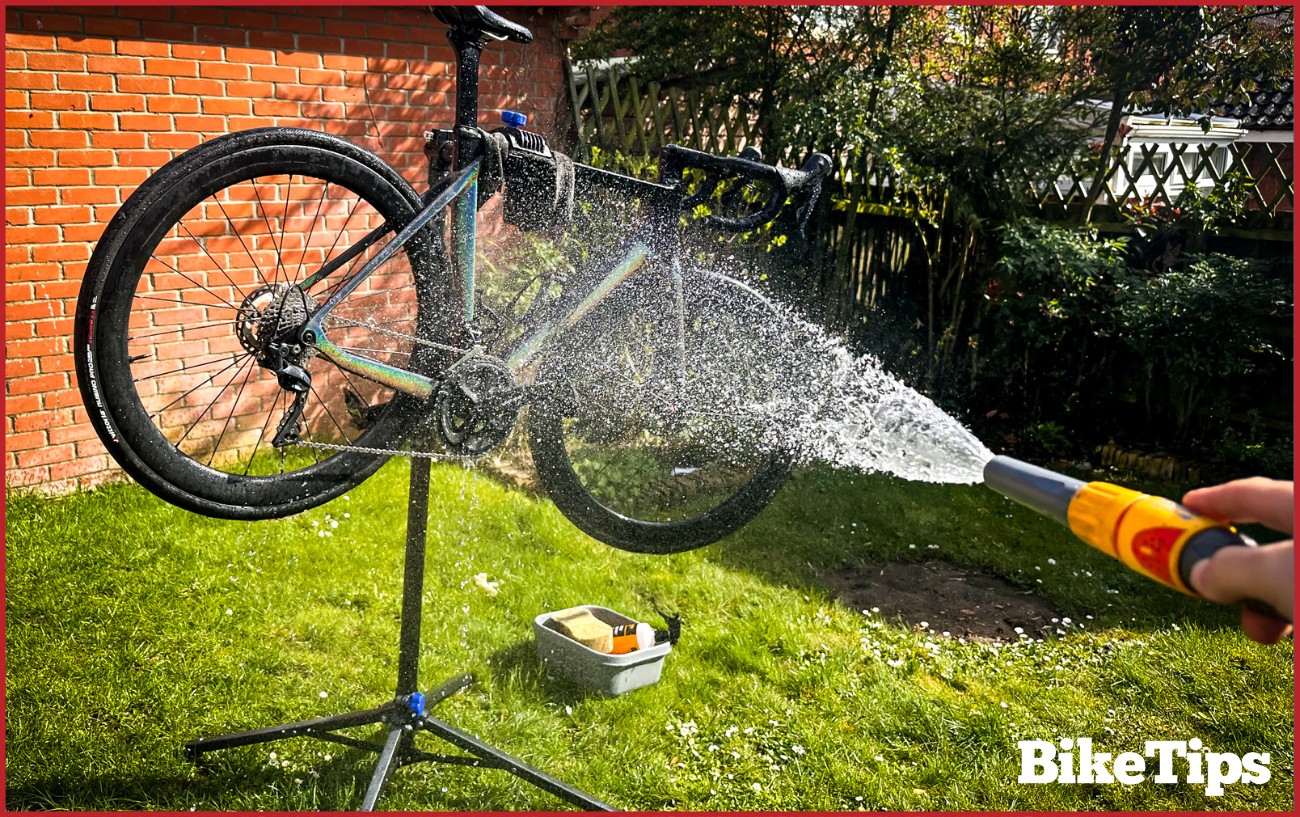 A road bike in a stand being rinsed with a hose.