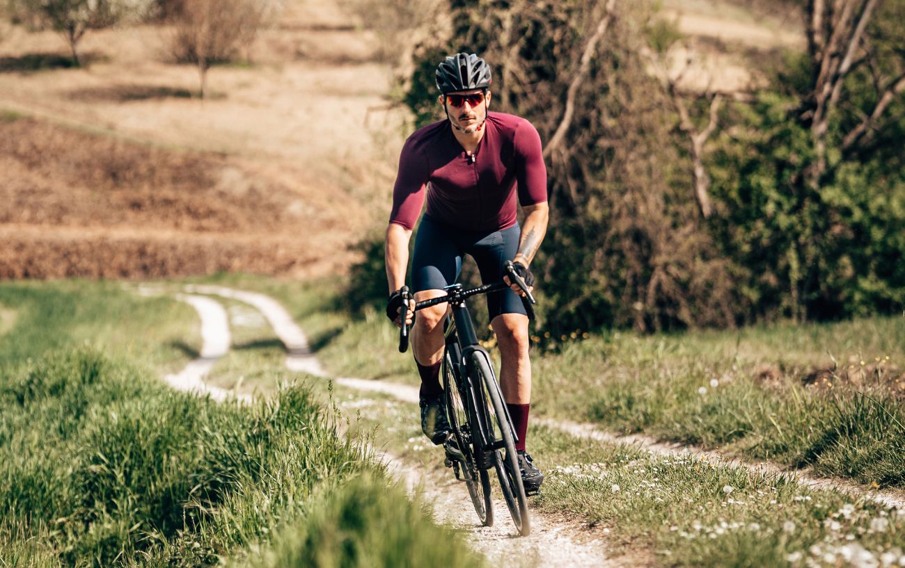 A cyclist in a burgundy jersey climbs a dirt path on a gravel bike.