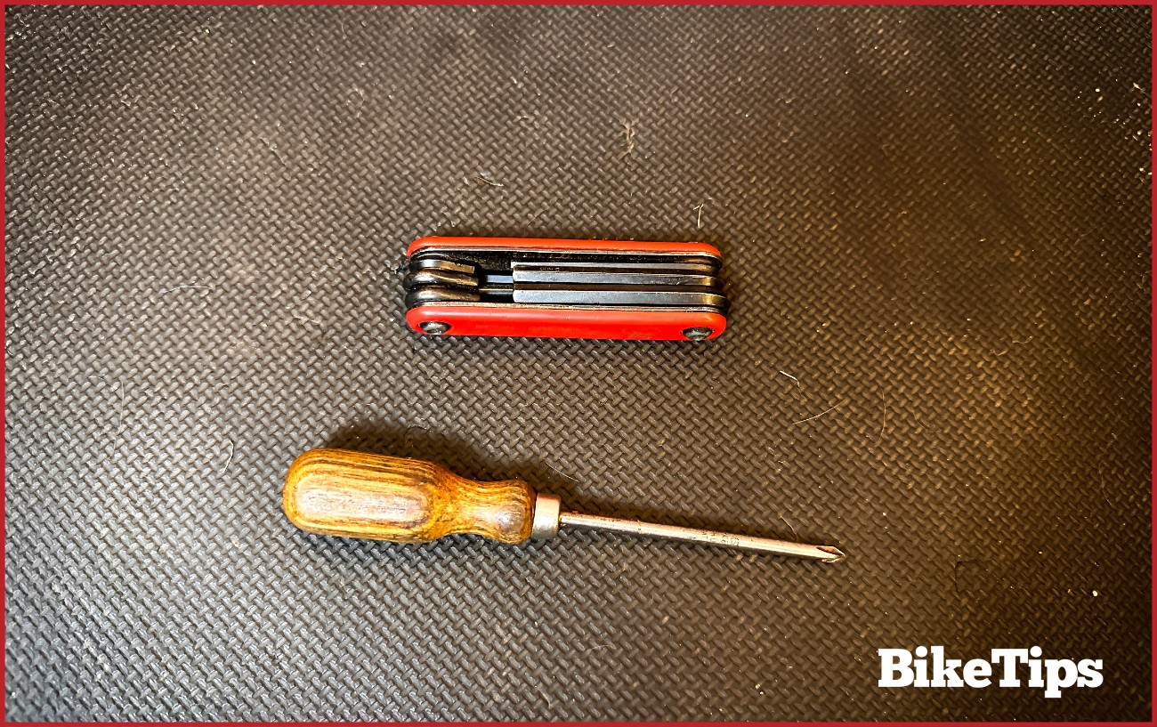 An Allen key set next to a screw driver on a padded mat floor.