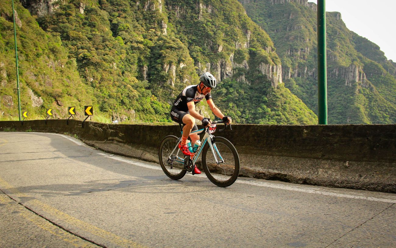 A cyclist climbs a steep mountain pass on a white road bike.