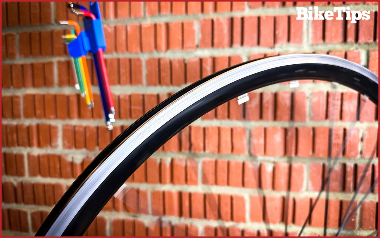Bike wheel spinning in a truing stand with hex keys hanging behind.