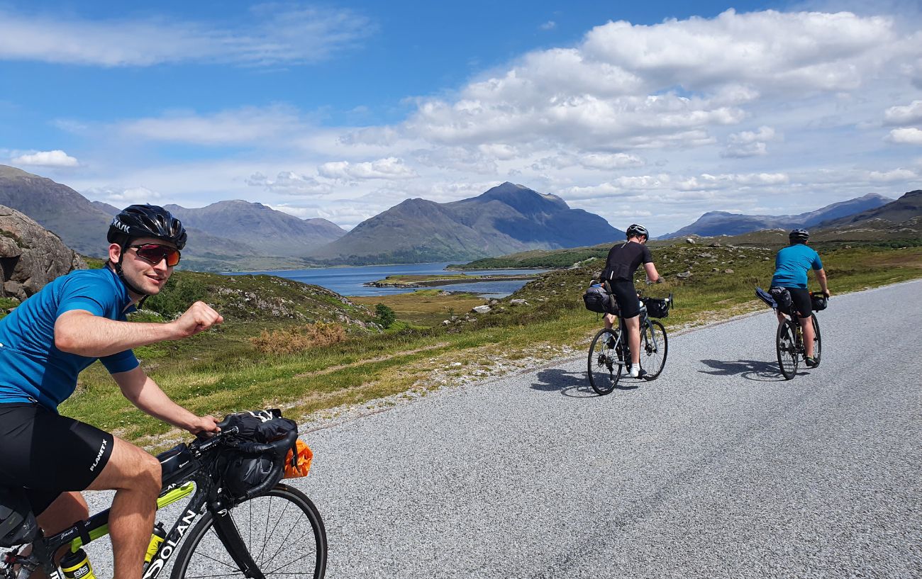 Cyclists climbing a road with Scottish lakes and mountains in the background.
