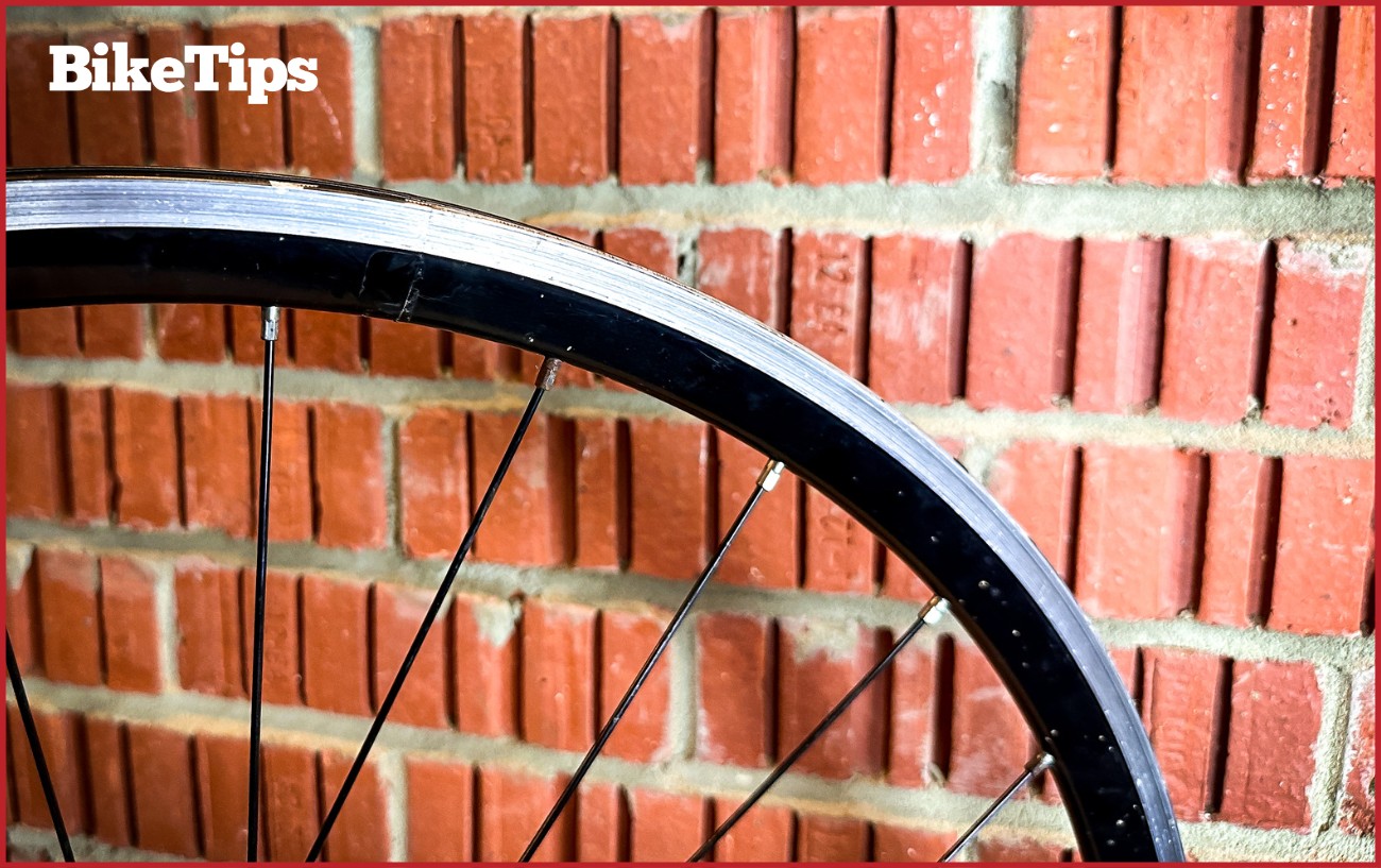 A bike wheel against a brick wall without a tire on.
