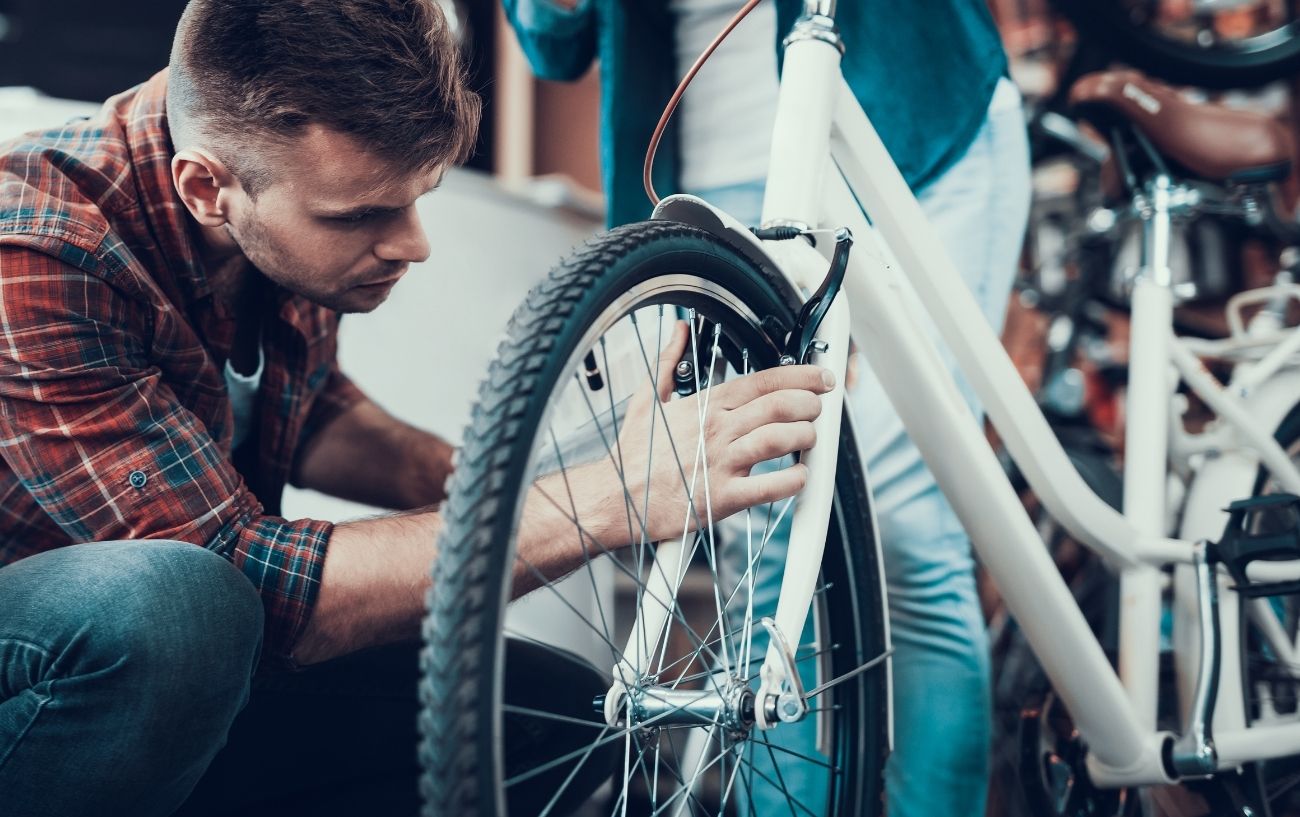 A cyclist adjusts the V brakes on a white hybrid bike.