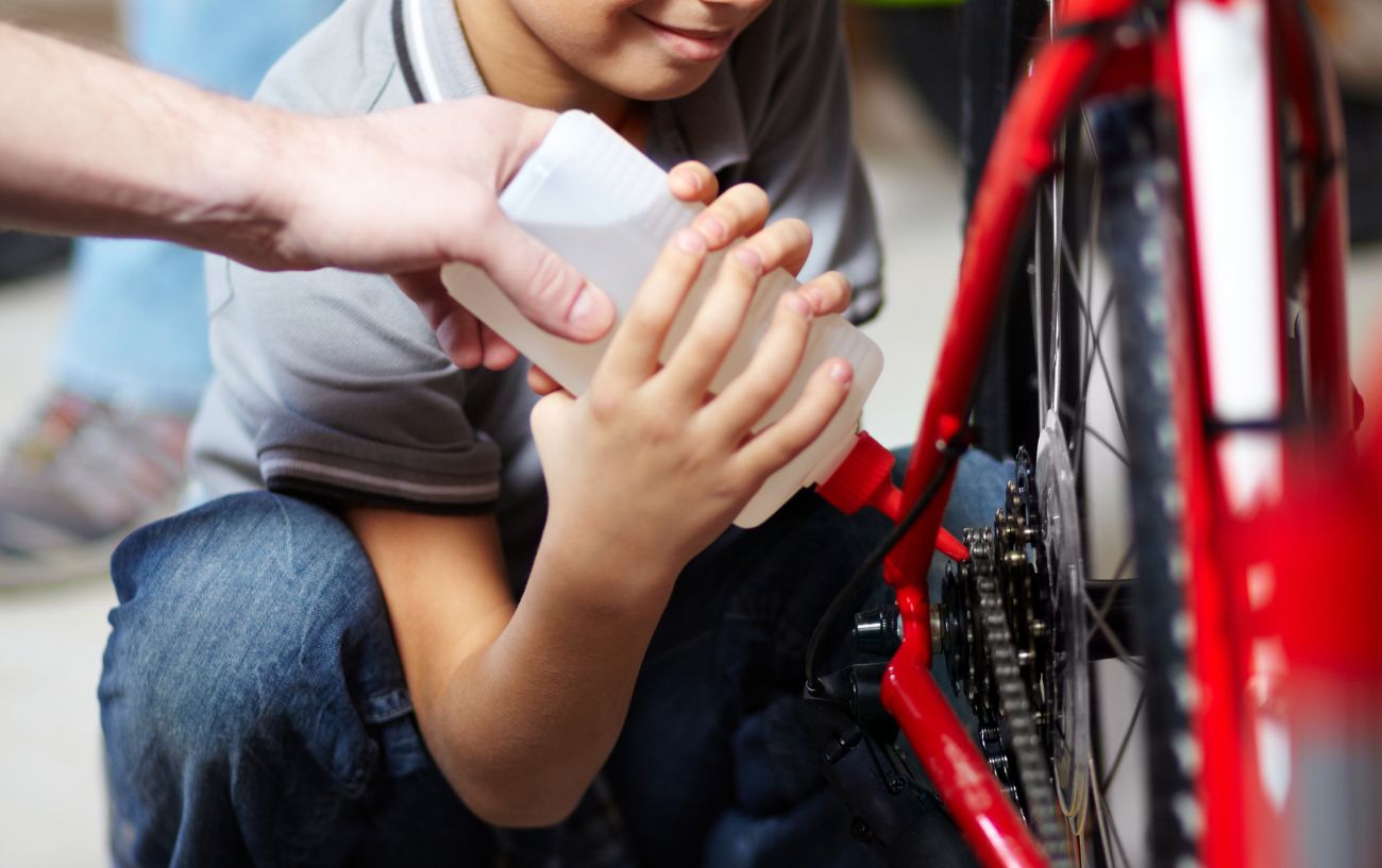 A child puts wet lube on his bike with help from his dad.