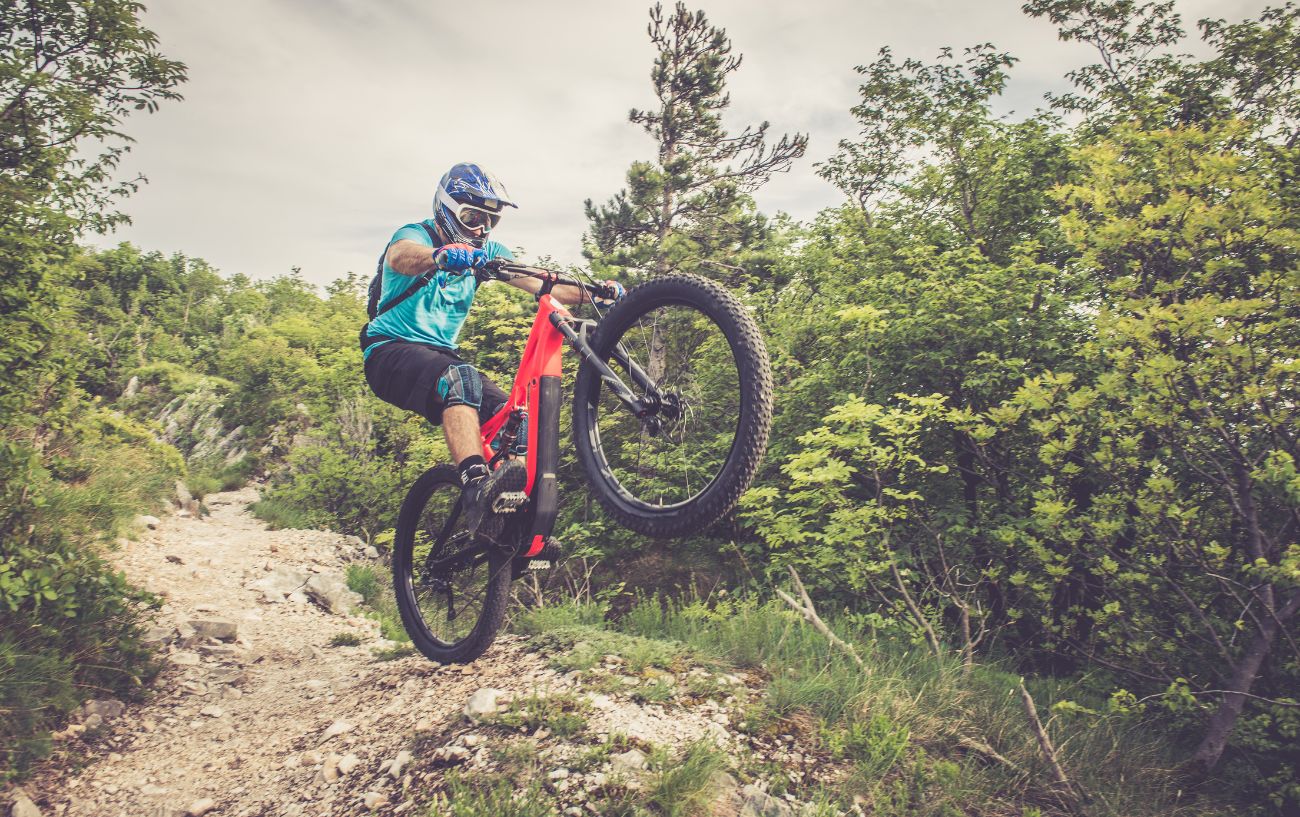 A downhill mountain biker pops a wheelie on a rocky trail.