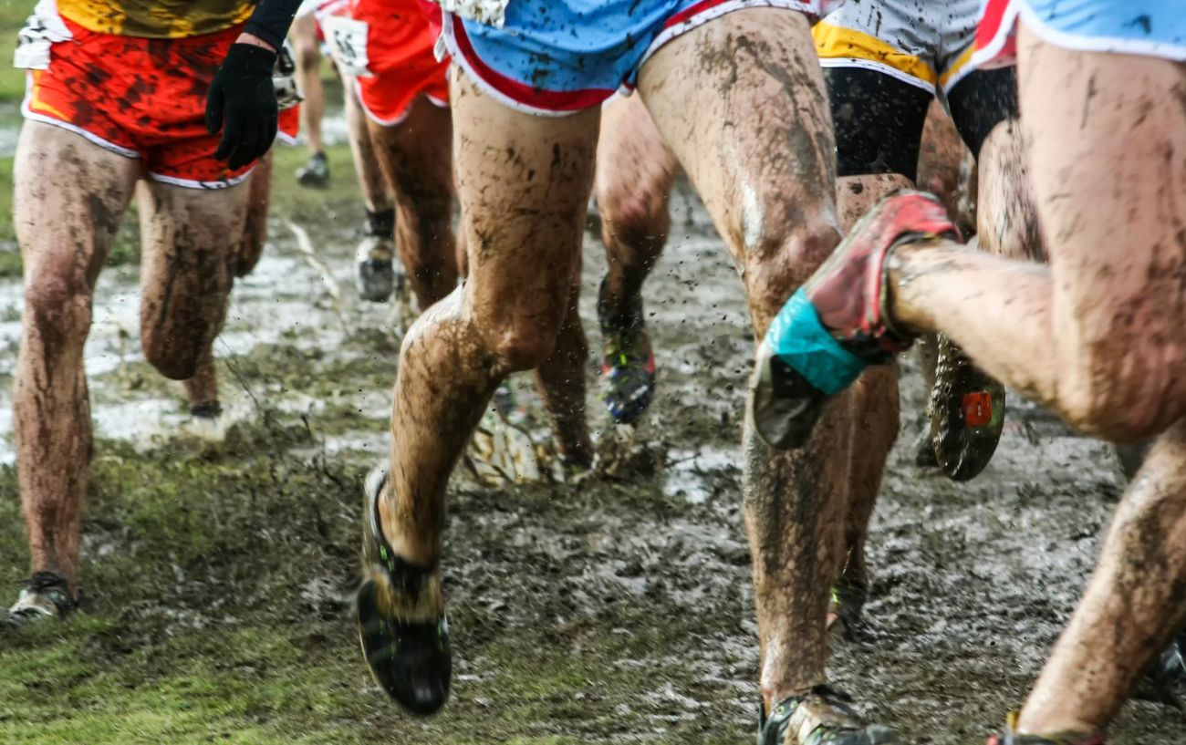A group of runners charge through a muddy field.
