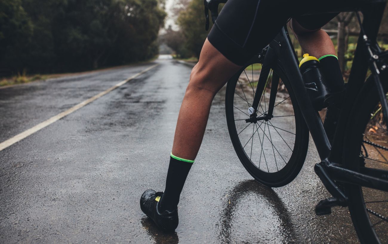 A cyclist puts their leg out on a wet road.