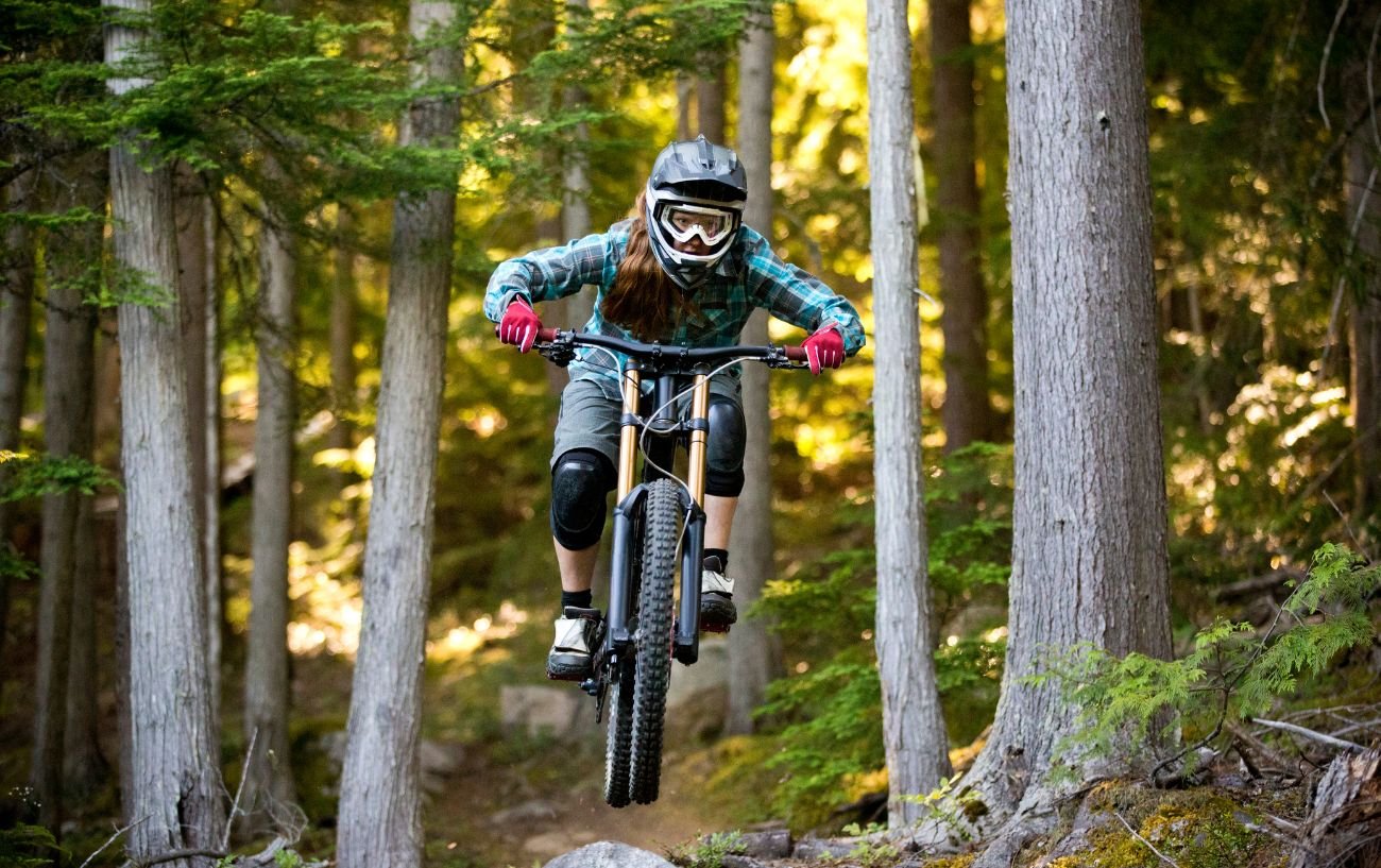 A cyclist flies through the air while downhill mountain biking in a forest.