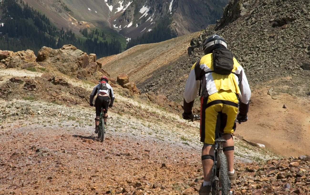 Two downhill mountain bikers descend a rocky hill face.