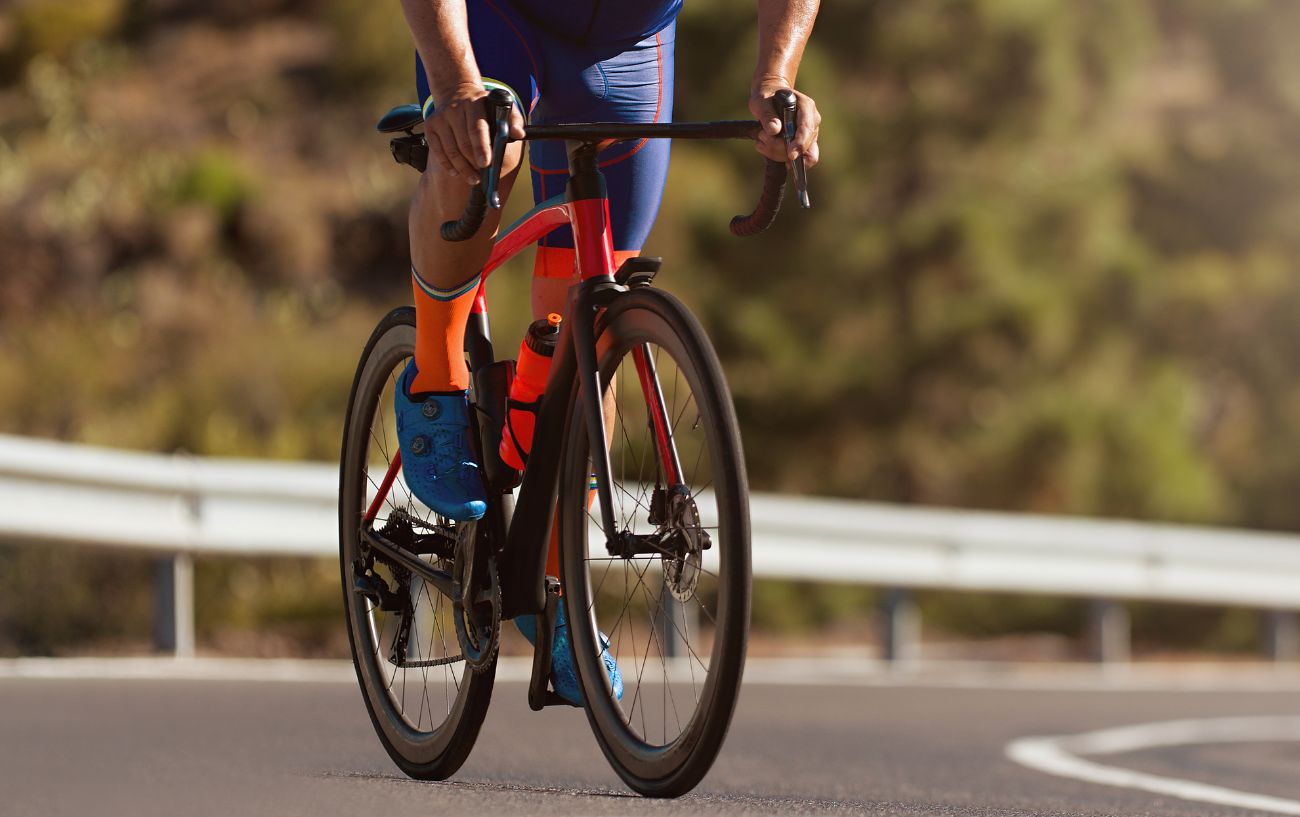 A cyclist climbs an asphalt road on an orange endurance road bike.