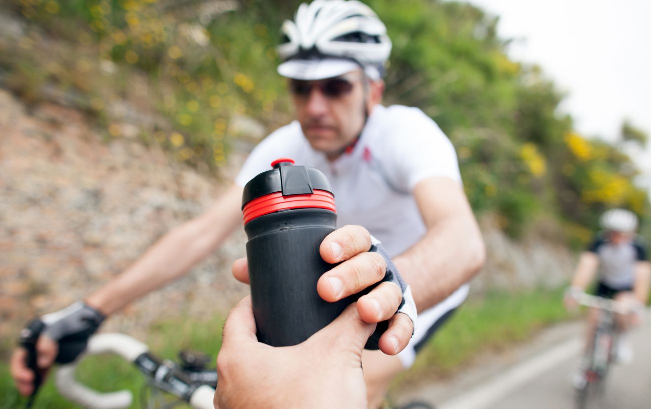 Cyclist gets handed a black and red water bottle to rehydrate.