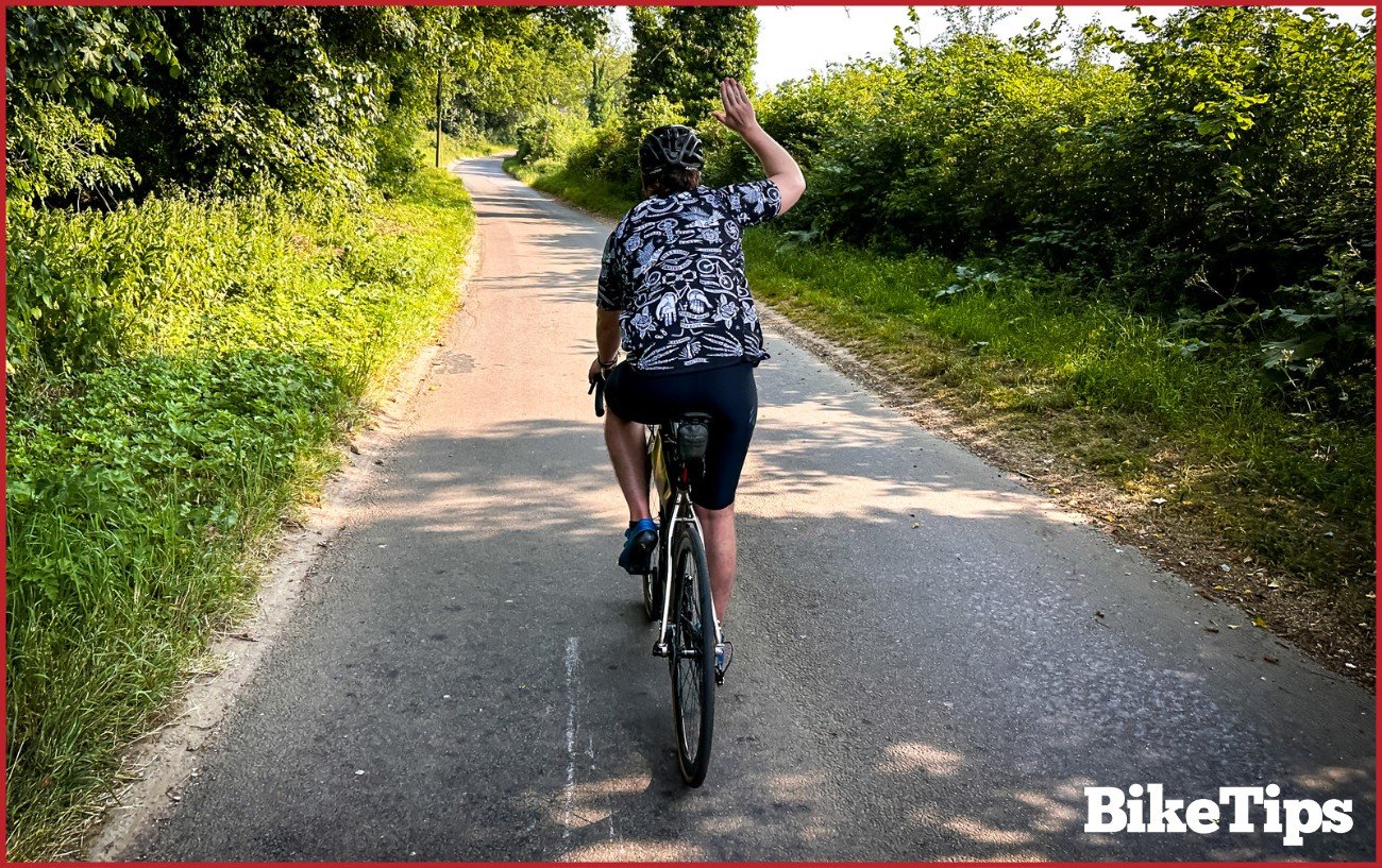 A cyclist showing a stopping signal while riding a road bike.