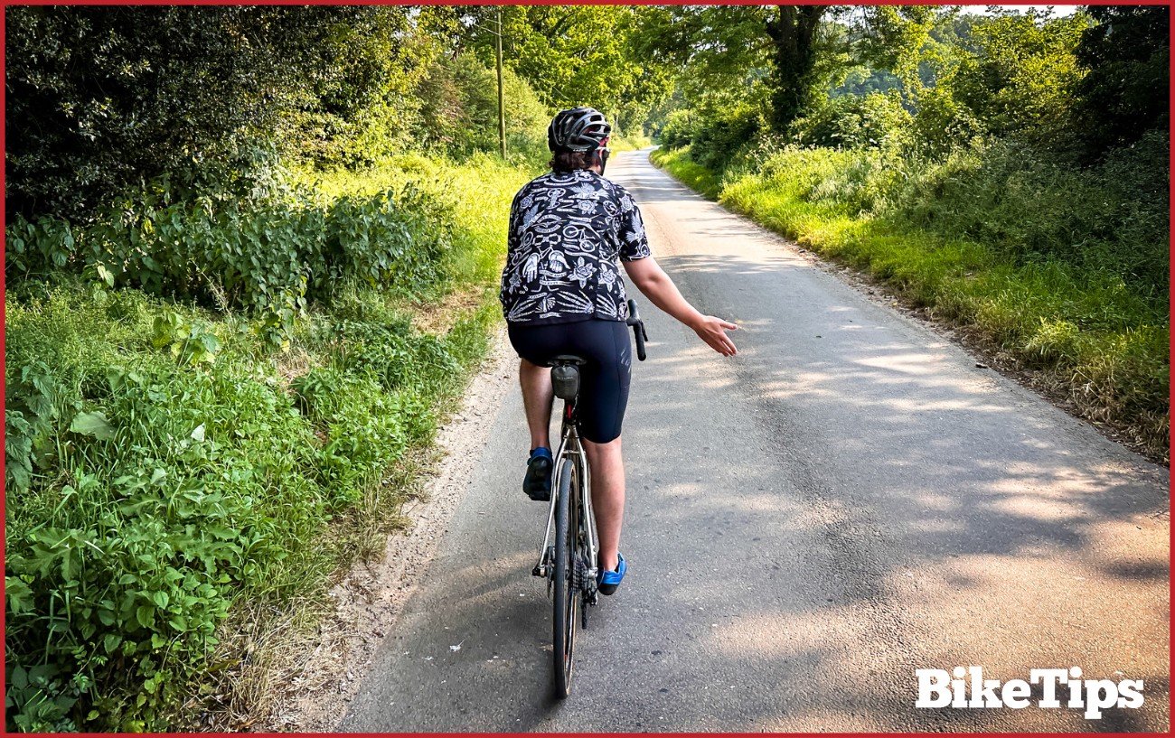 A cyclist showing a go ahead signal while riding a road bike.