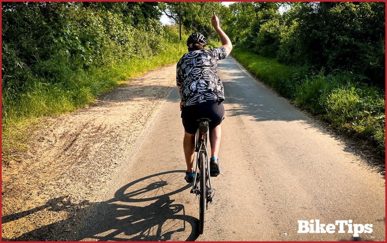 A cyclist showing a straight on signal while riding a road bike.