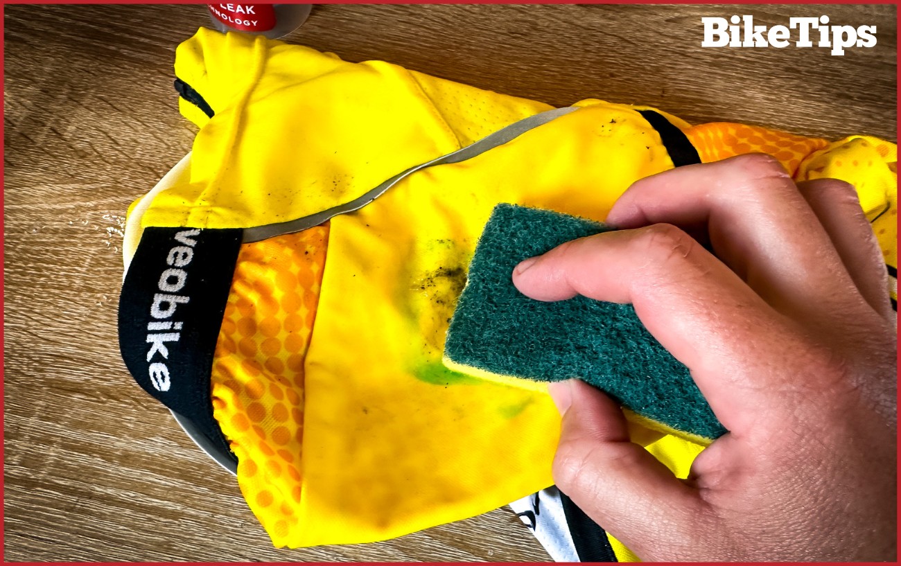 Scrubbing dishwashing liquid into a bike jersey using a sponge.