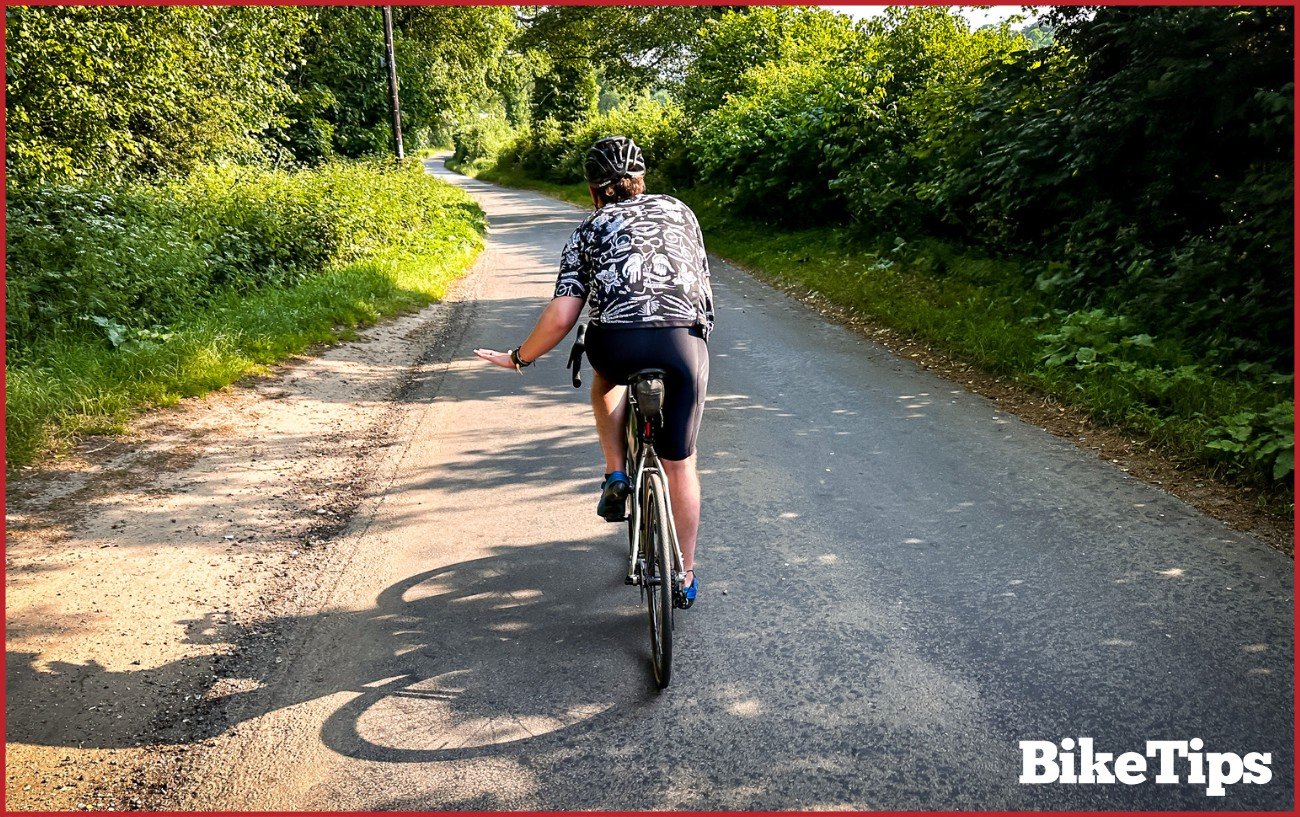A cyclist showing slowing down signal while riding a road bike.