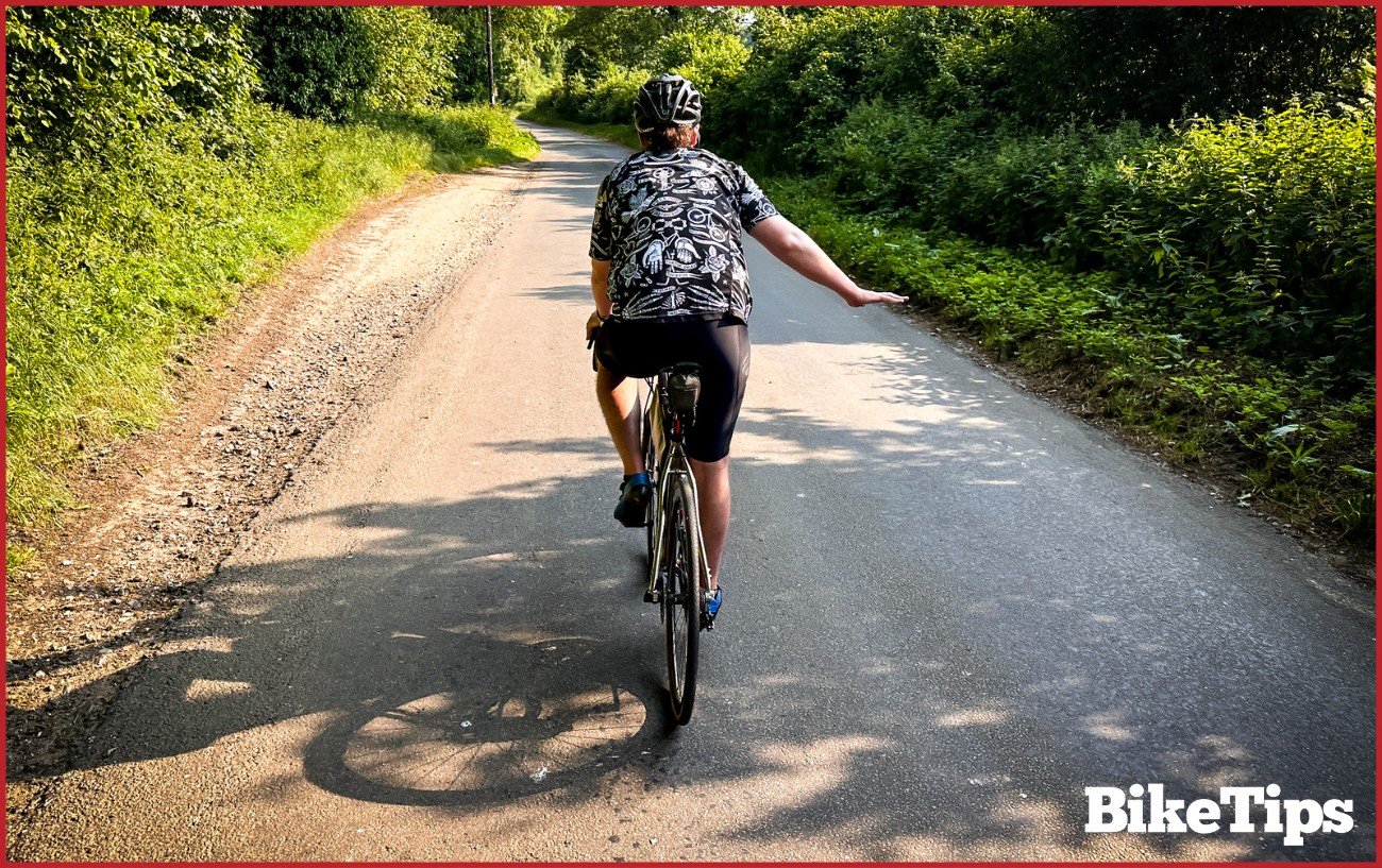 A cyclist showing a rough terrain signal while riding a road bike.