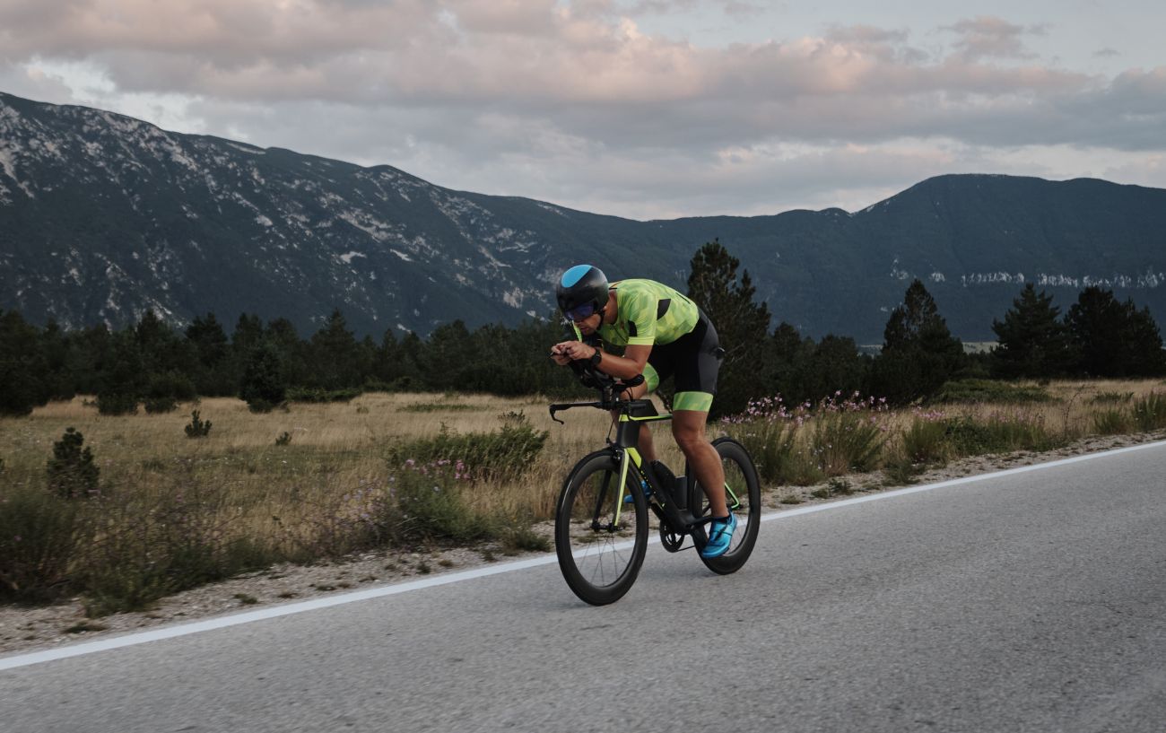 The Science of Cycling: How Top Athletes Prepare For The Tour De France 3 Cyclist wearing green and black rides a time trial bike with mountains in the background.