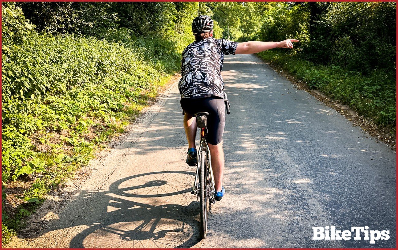 A cyclist showing a right hand turn signal while riding a road bike.