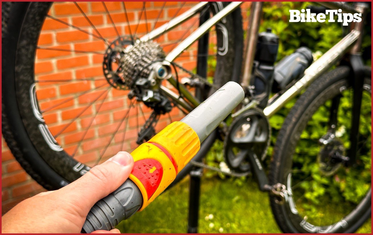 A hose pointing to a bike which is about to be rinsed. 