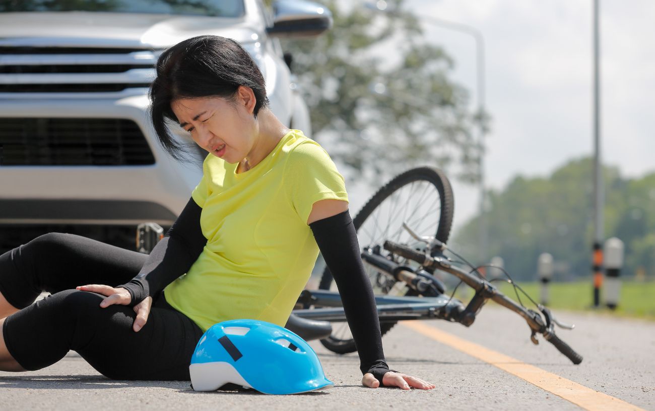 Cyclist wearing a yellow top sits on the road after an accident.