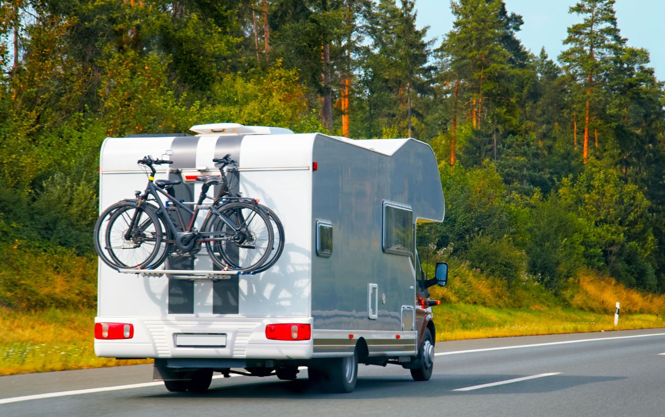 Campervan drives along road with two bikes attached to the back. 
