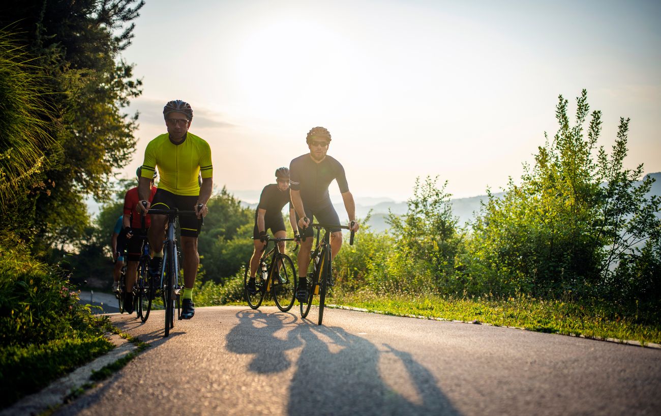 A group of cyclists ride along a country road at sunset.