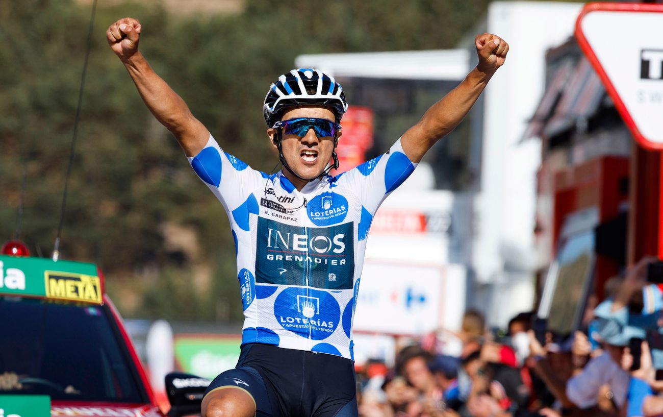 Carapaz celebrating a stage win in a blue polka-dot jersey.