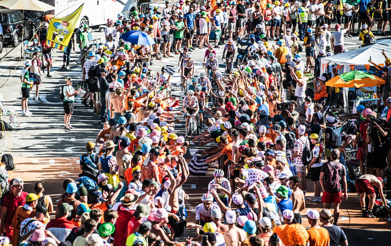 A wide-angle shot of Tour de France riders climbing through an alleyway formed of spectators.